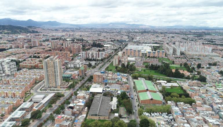 se observa la ciudad de Bogotá desde las alturas. Además, se ven casas, edificios, calles, automóviles, buses, entre otros.